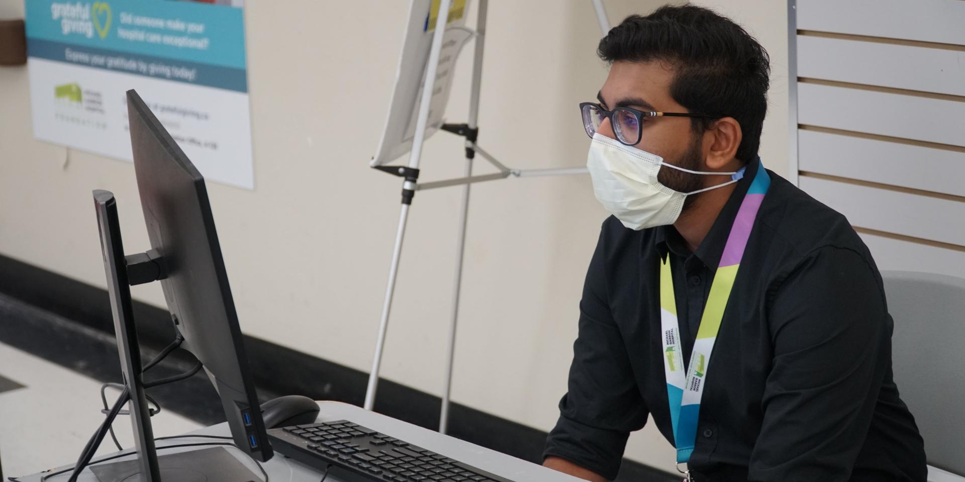 Screener Piranavvan Nagarajan wears a mask in front of a computer
