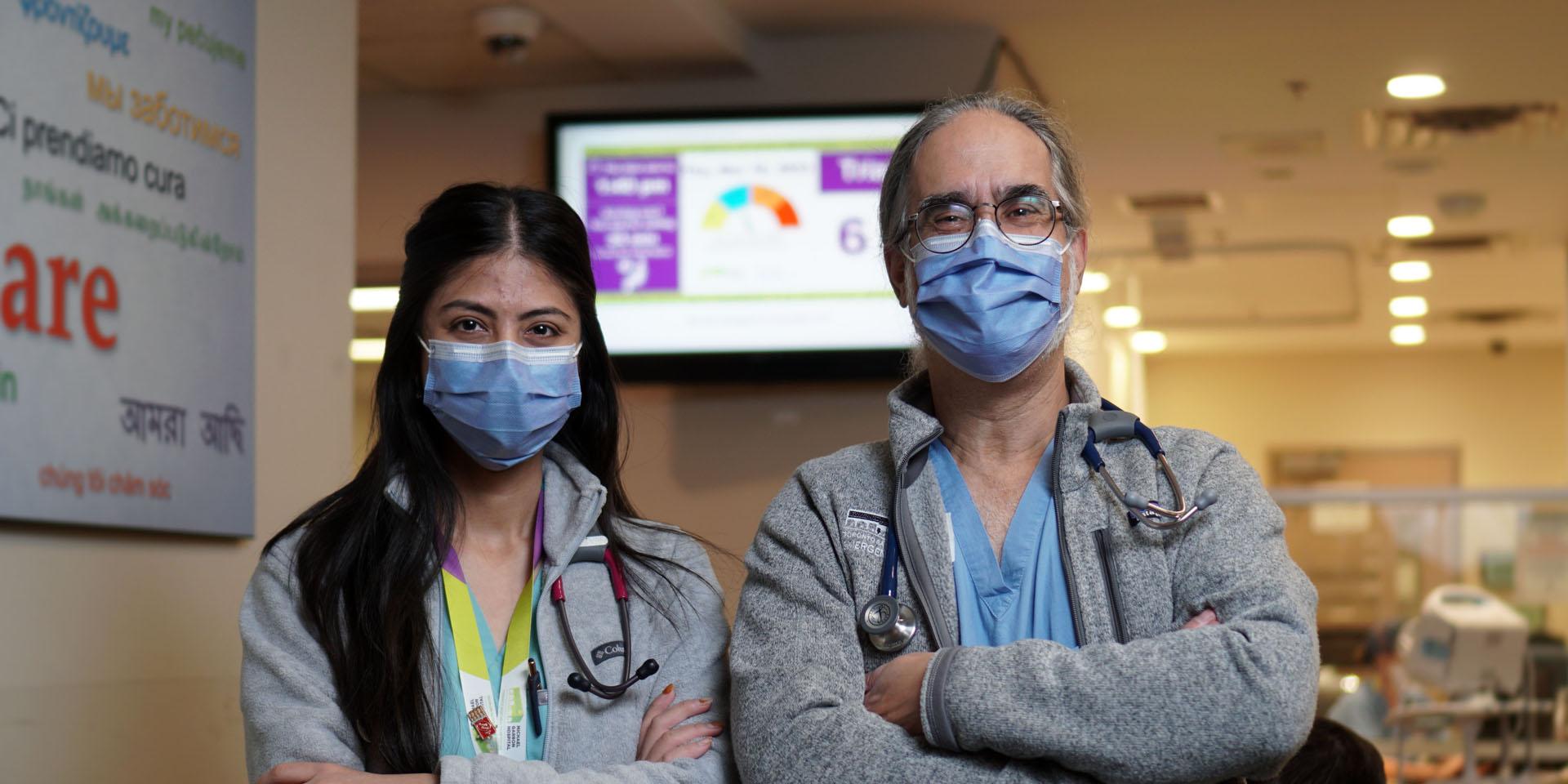 A nurse and doctor stand in front of a wait time clock in Michael Garron Hospital's Emergency Department.