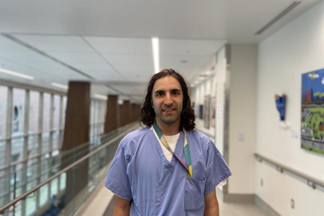 Dr. Christopher Kandel, Michael Garron Hospital A man wearing hospital scrubs is standing in the hallway of a hospital looking directly at the camera.