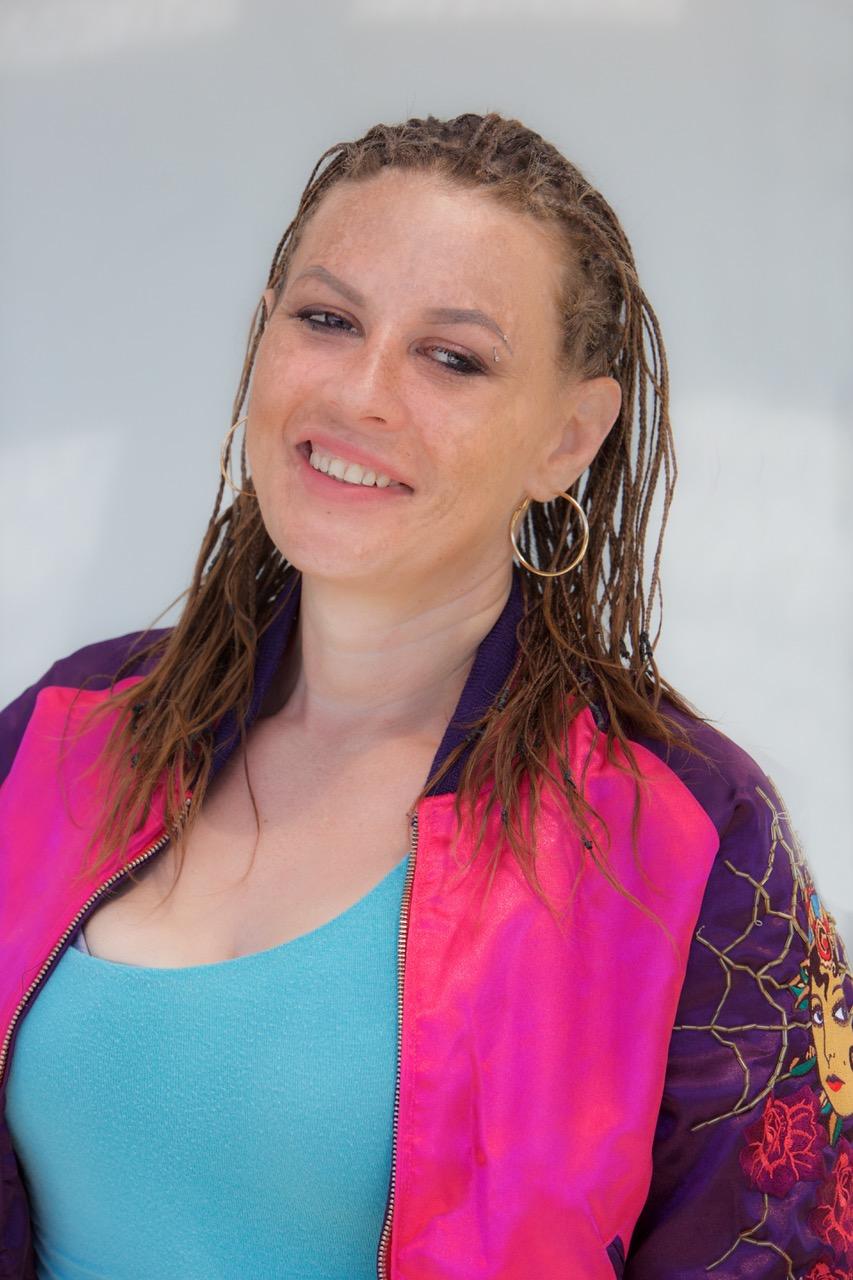 A smiling woman wearing a blue shirt and pink jacket.